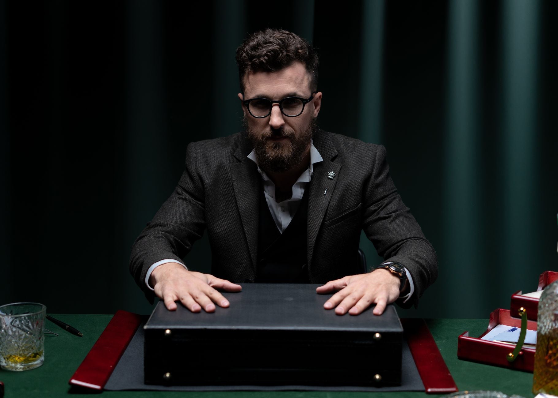 Bearded man in black suit seated at a table with briefcase, symbolizing professionalism and confidence.