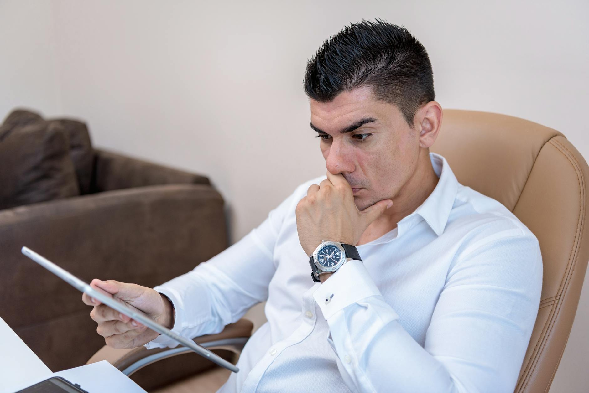 Man in white shirt intently using a tablet in a contemporary office setting.