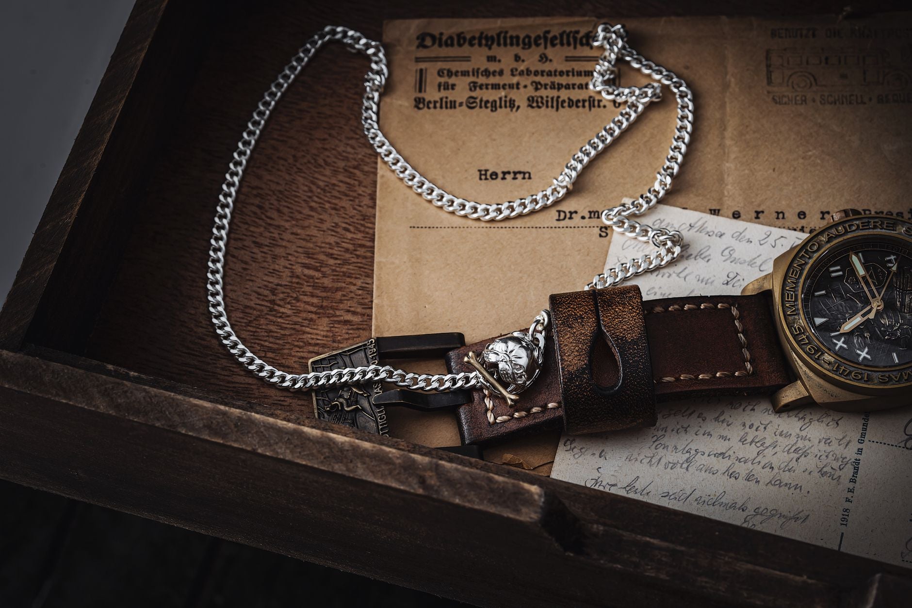 A rustic display featuring a watch, chain, and antique letters in a wooden box, showcasing vintage charm.
