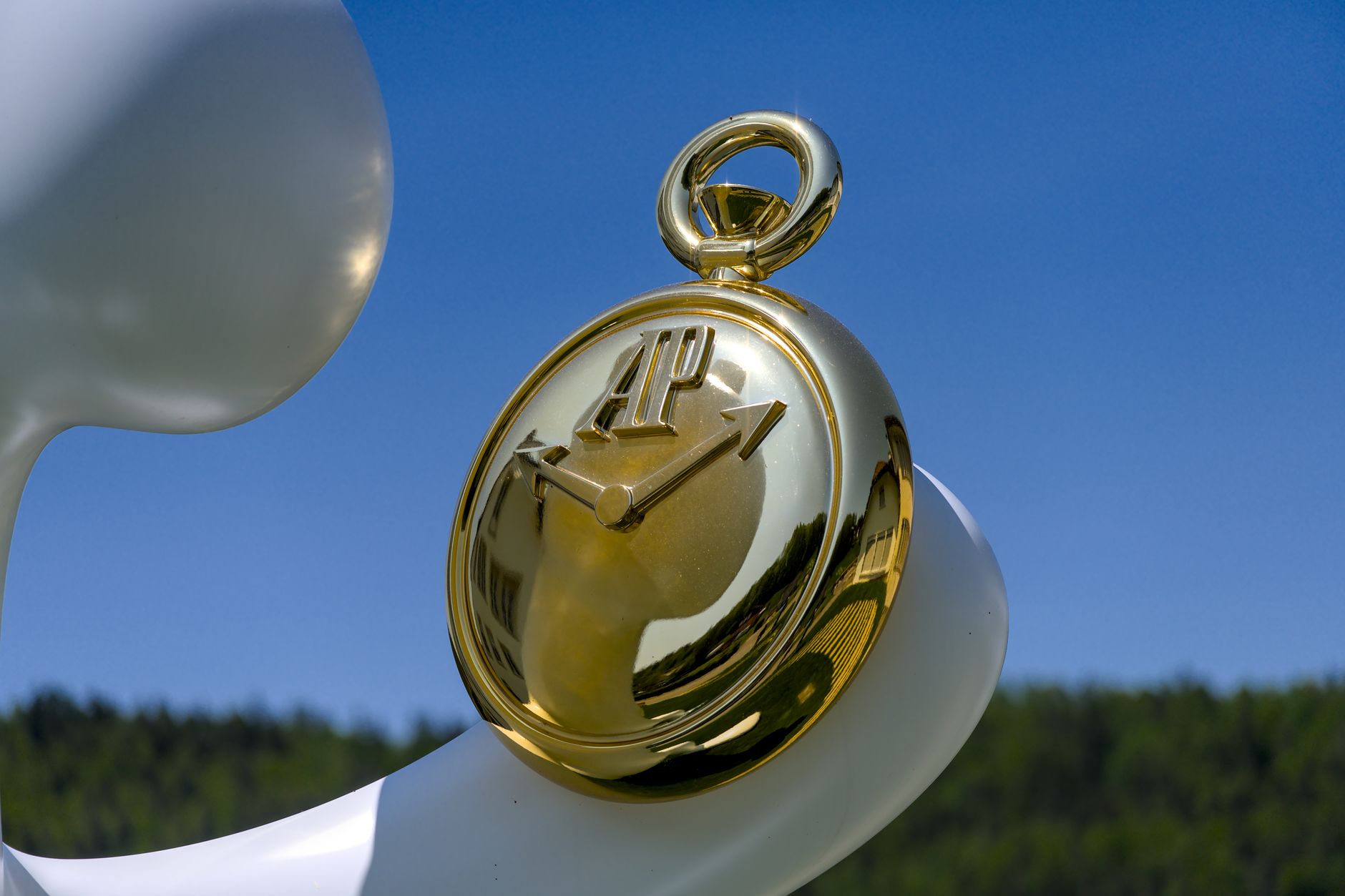 Close-up of a golden pocket watch set against a sunny blue sky, reflecting artistic elegance.