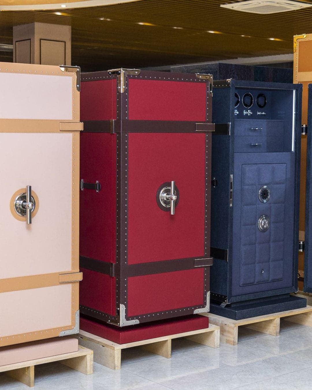 Three trunk-style safes side by side in cream, red and blue