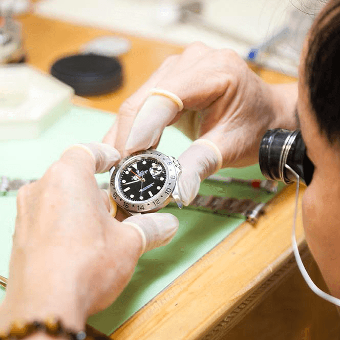 A watchmaker examining a movement through a loupe at the bench