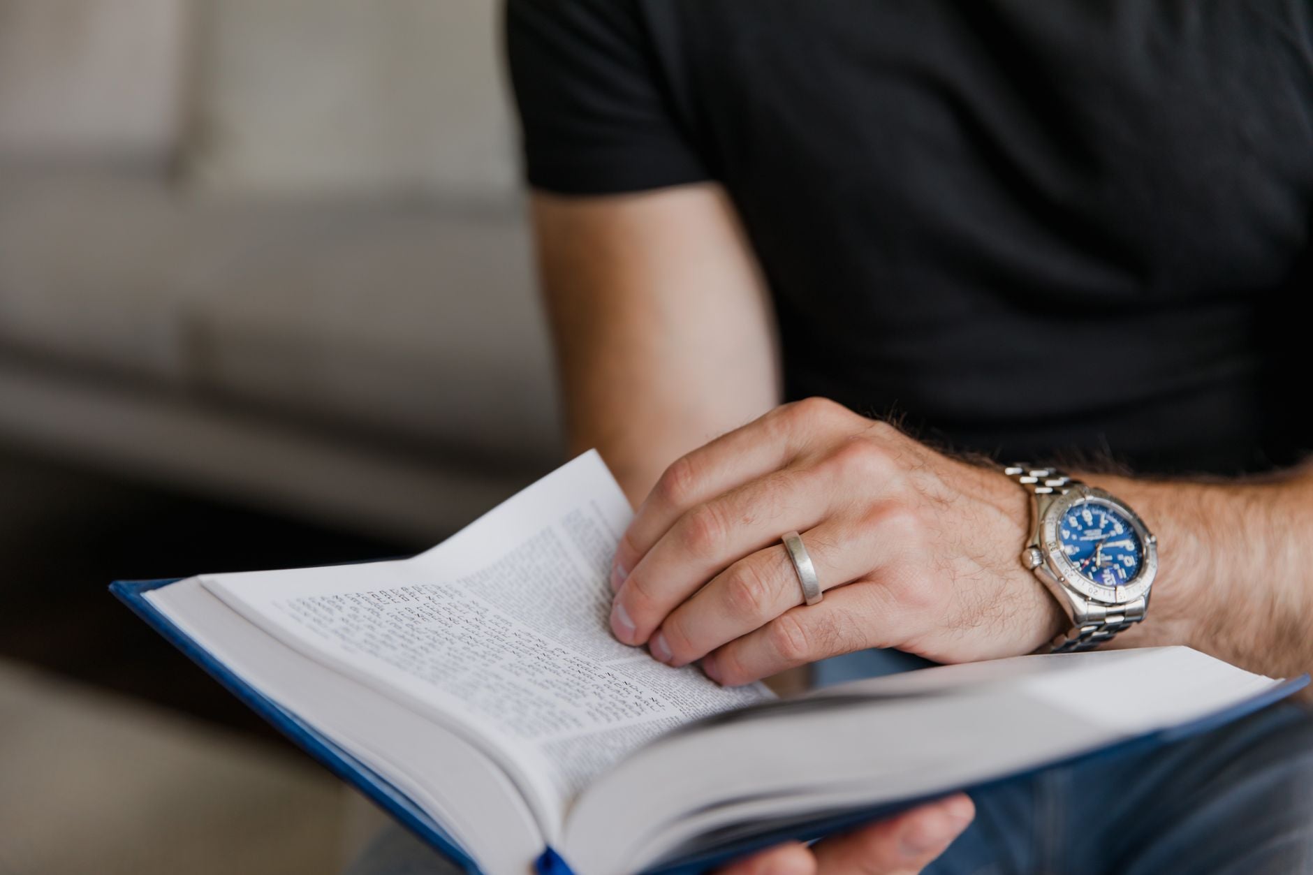 Man's hand with a wristwatch holding an open book, close-up.