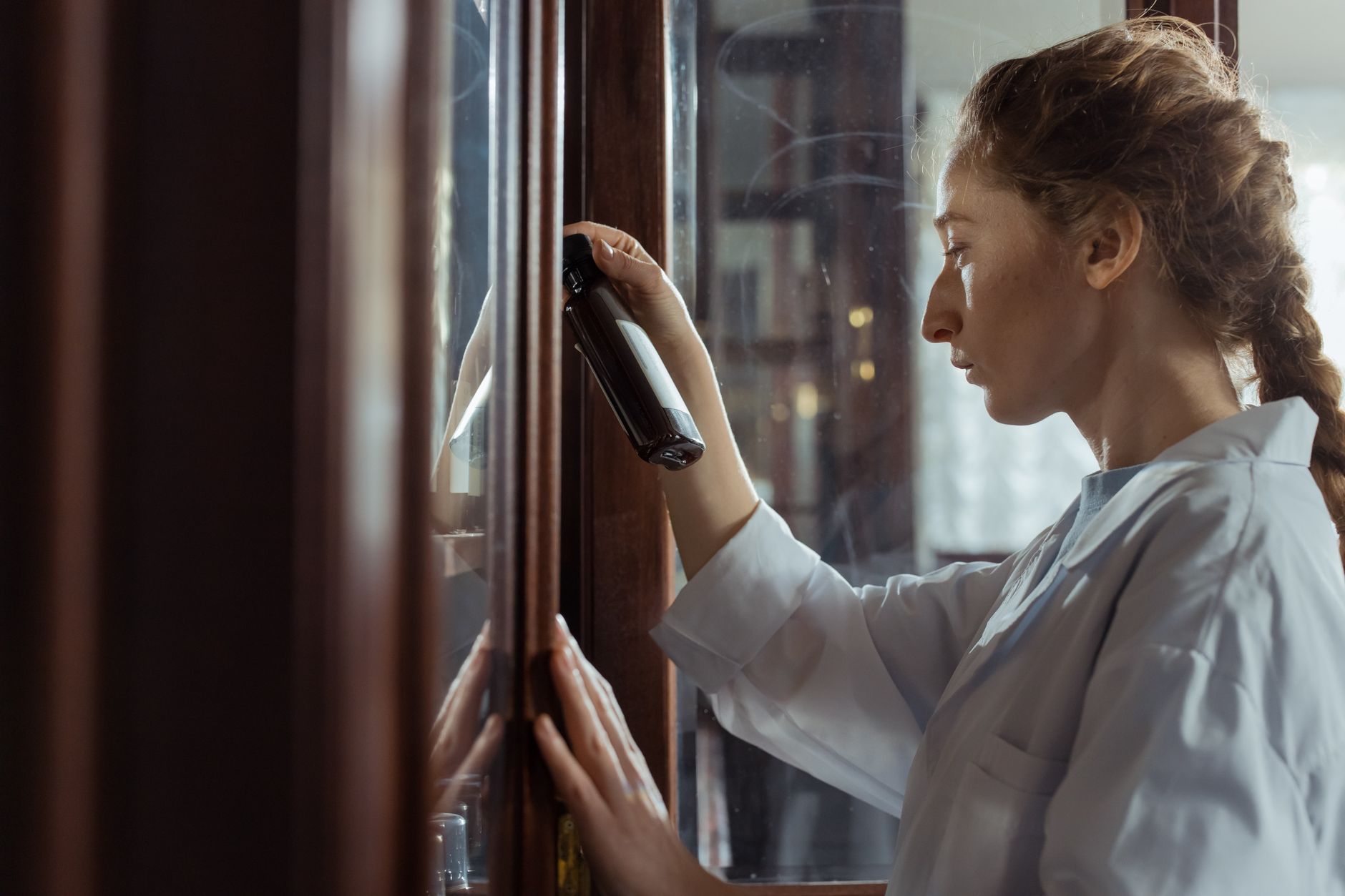 Focused woman inspecting cabinet with bottle in hand, indoors.