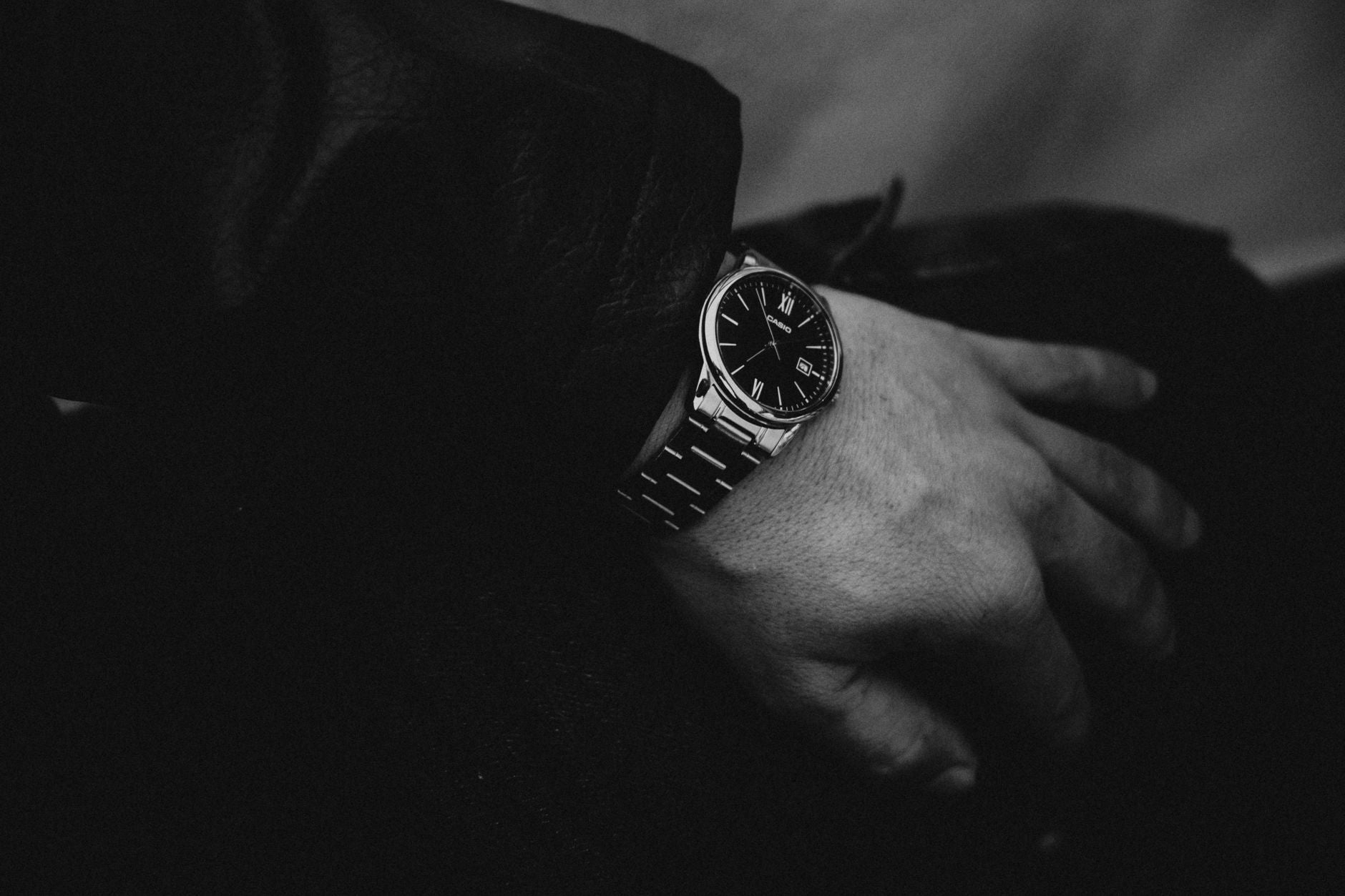 Monochrome close-up of a stylish wristwatch with Roman numerals on an adult's wrist.