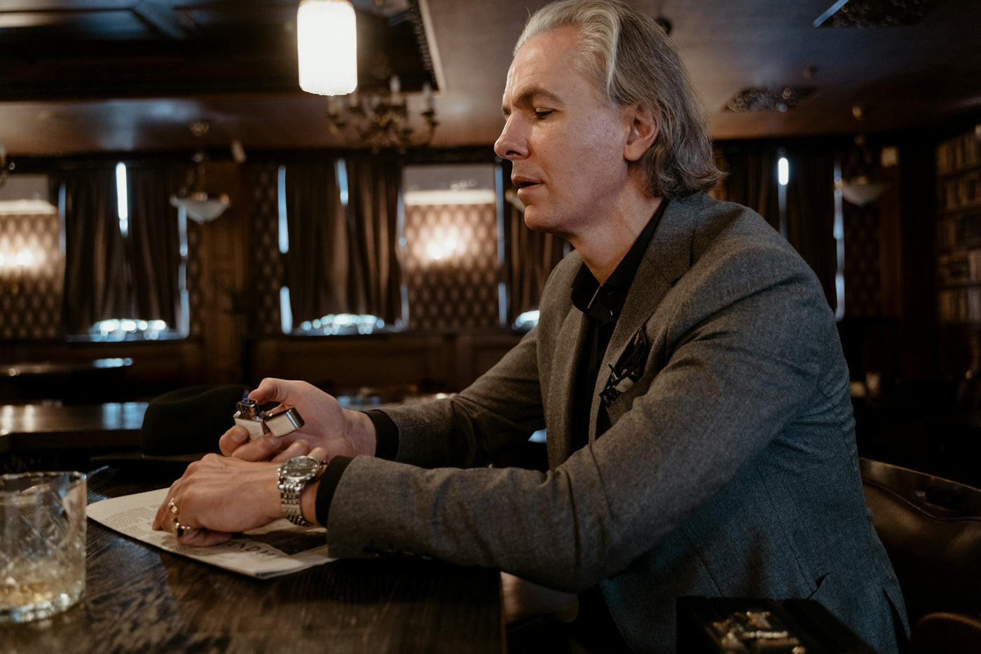 Senior man in a gray coat enjoying leisure time in a cozy indoor setting with ambient lighting.
