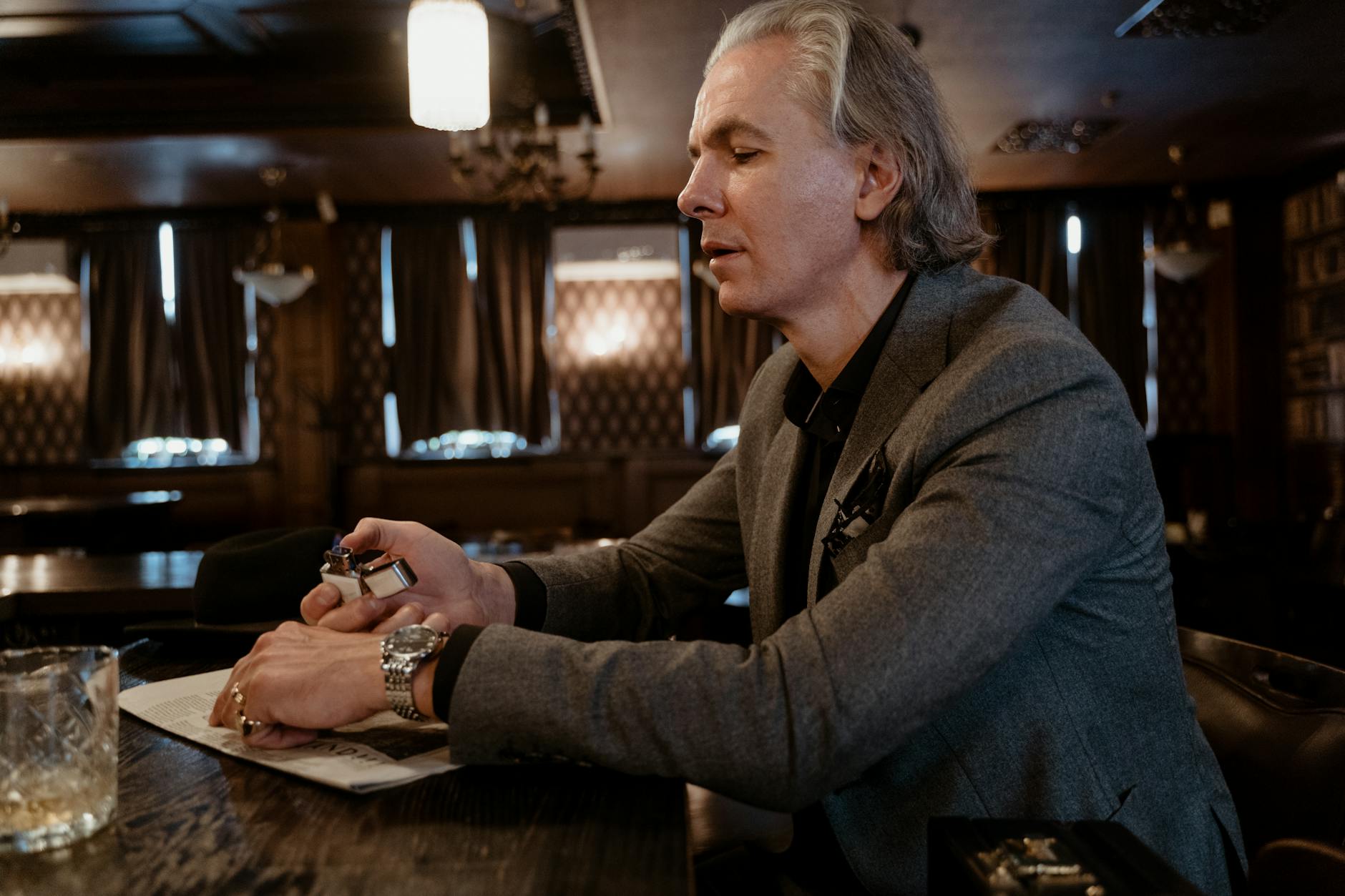 Senior man in a gray coat enjoying leisure time in a cozy indoor setting with ambient lighting.