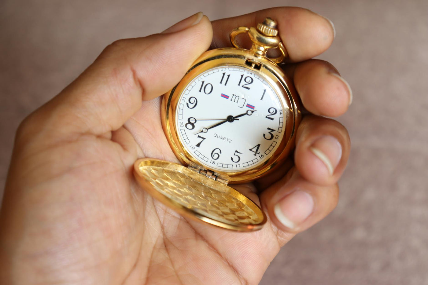 Close-up of a classic gold pocket watch held in a hand, showcasing vintage elegance.