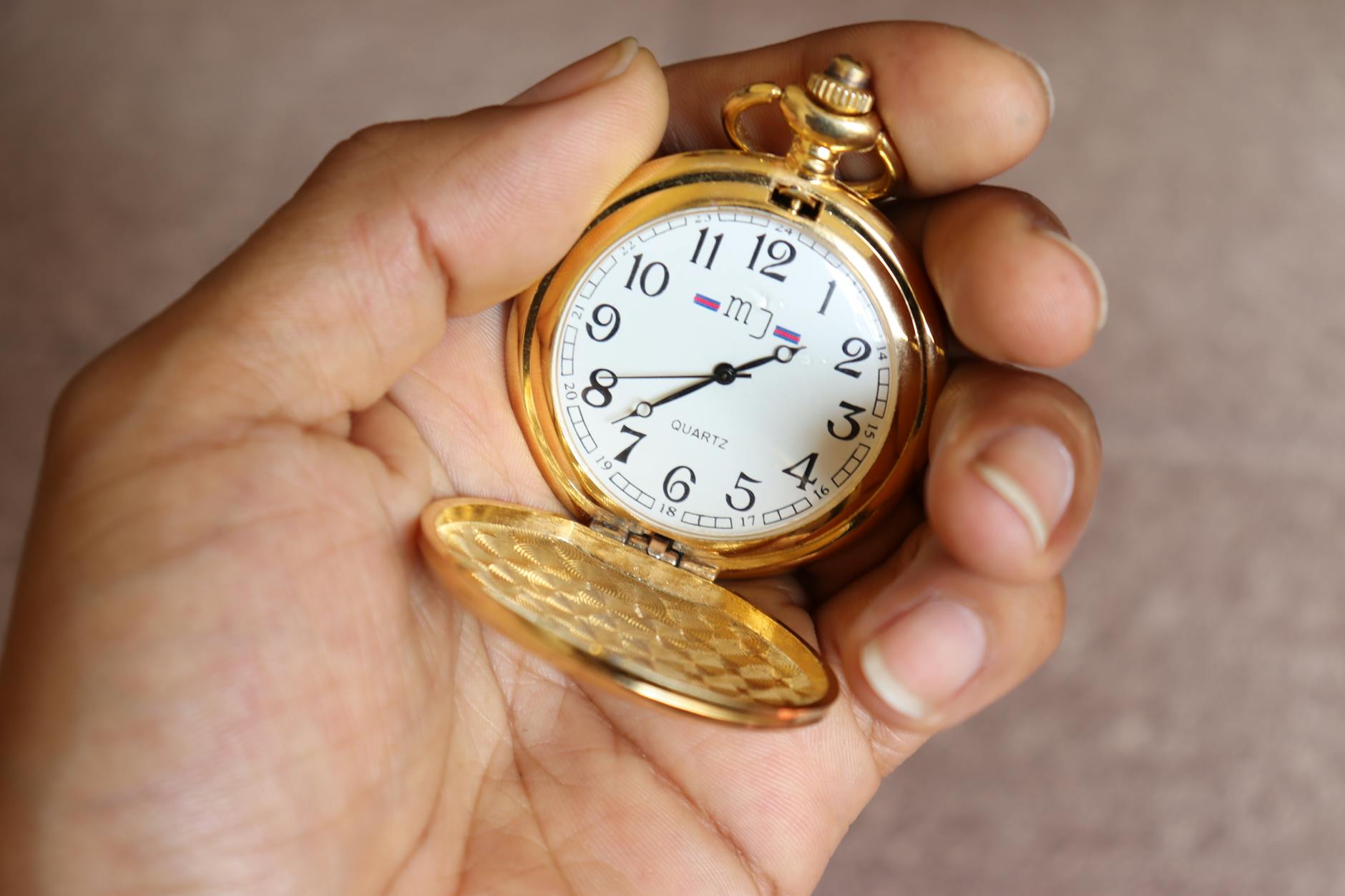 Close-up of a classic gold pocket watch held in a hand, showcasing vintage elegance.