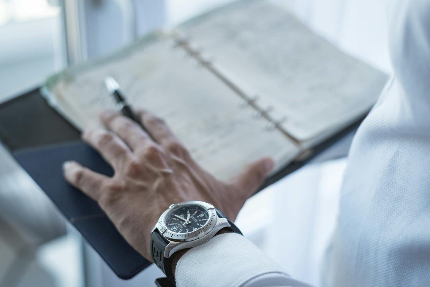 Close-up of a man holding a planner with a watch on his wrist, symbolizing time management.