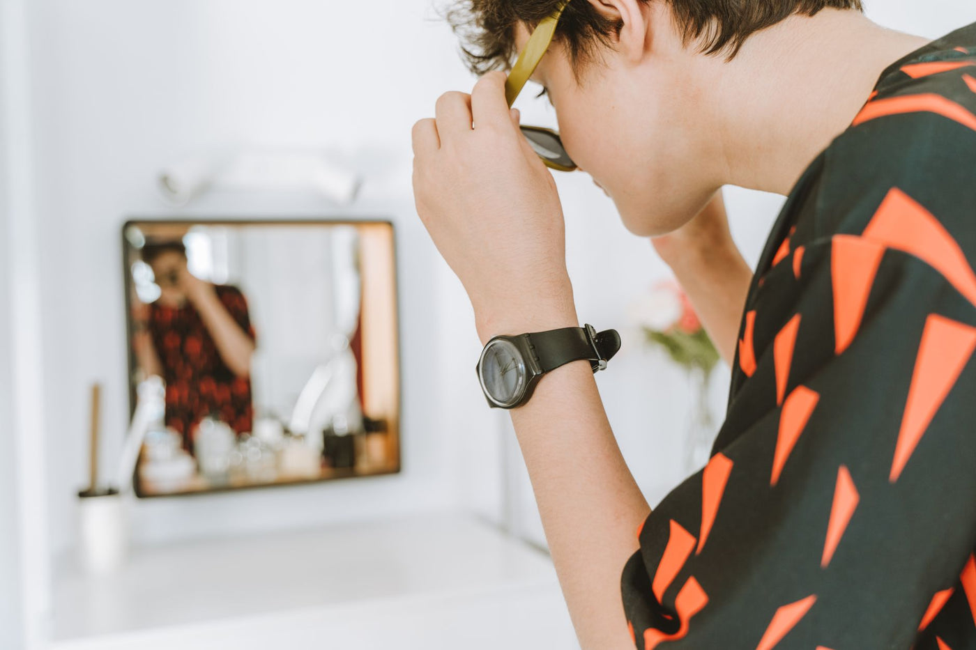 A stylish teenager adjusts sunglasses while looking in a mirror, embodying modern fashion trends.