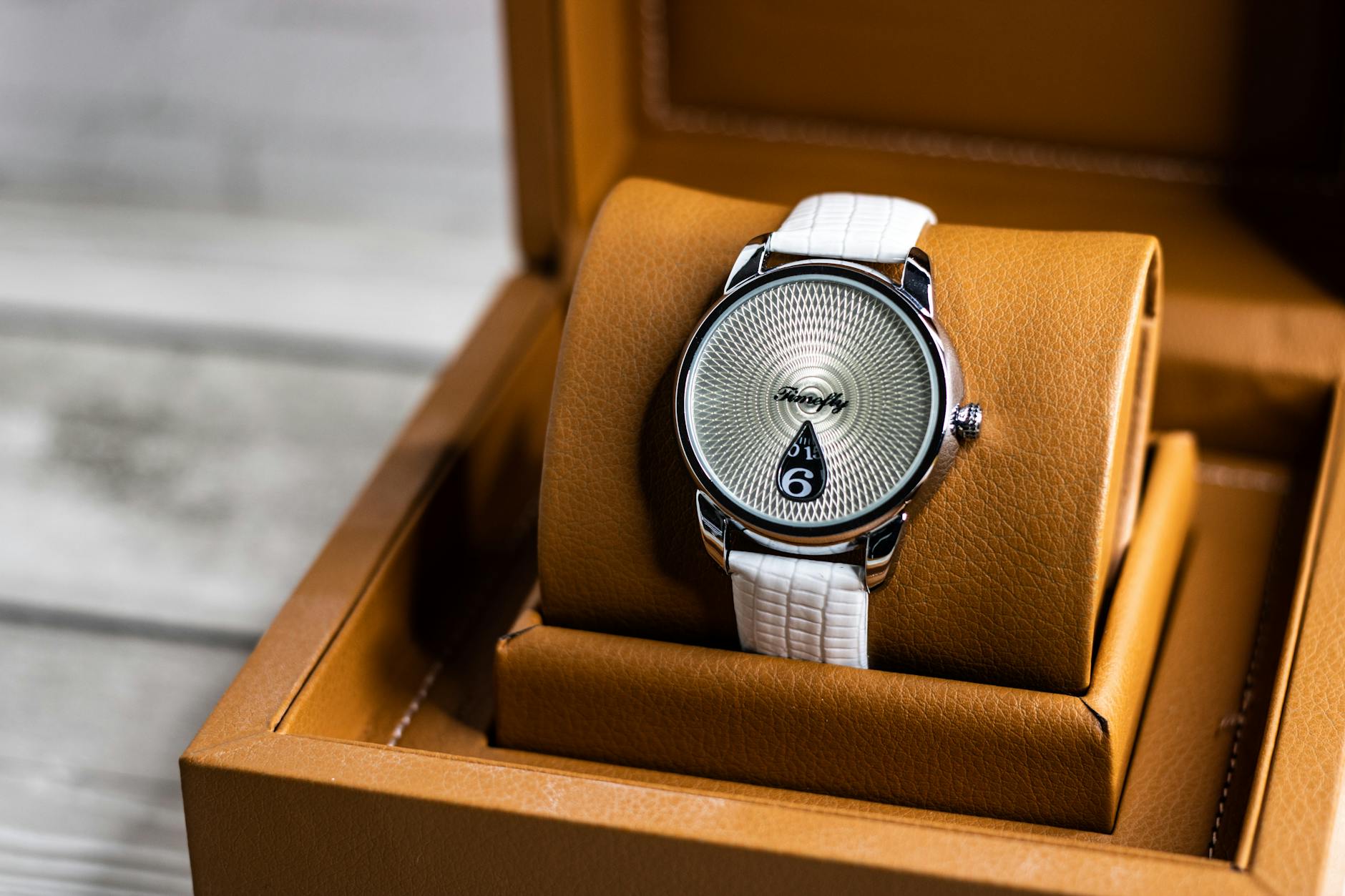 Close-up of a luxury watch with white strap in a brown leather box.