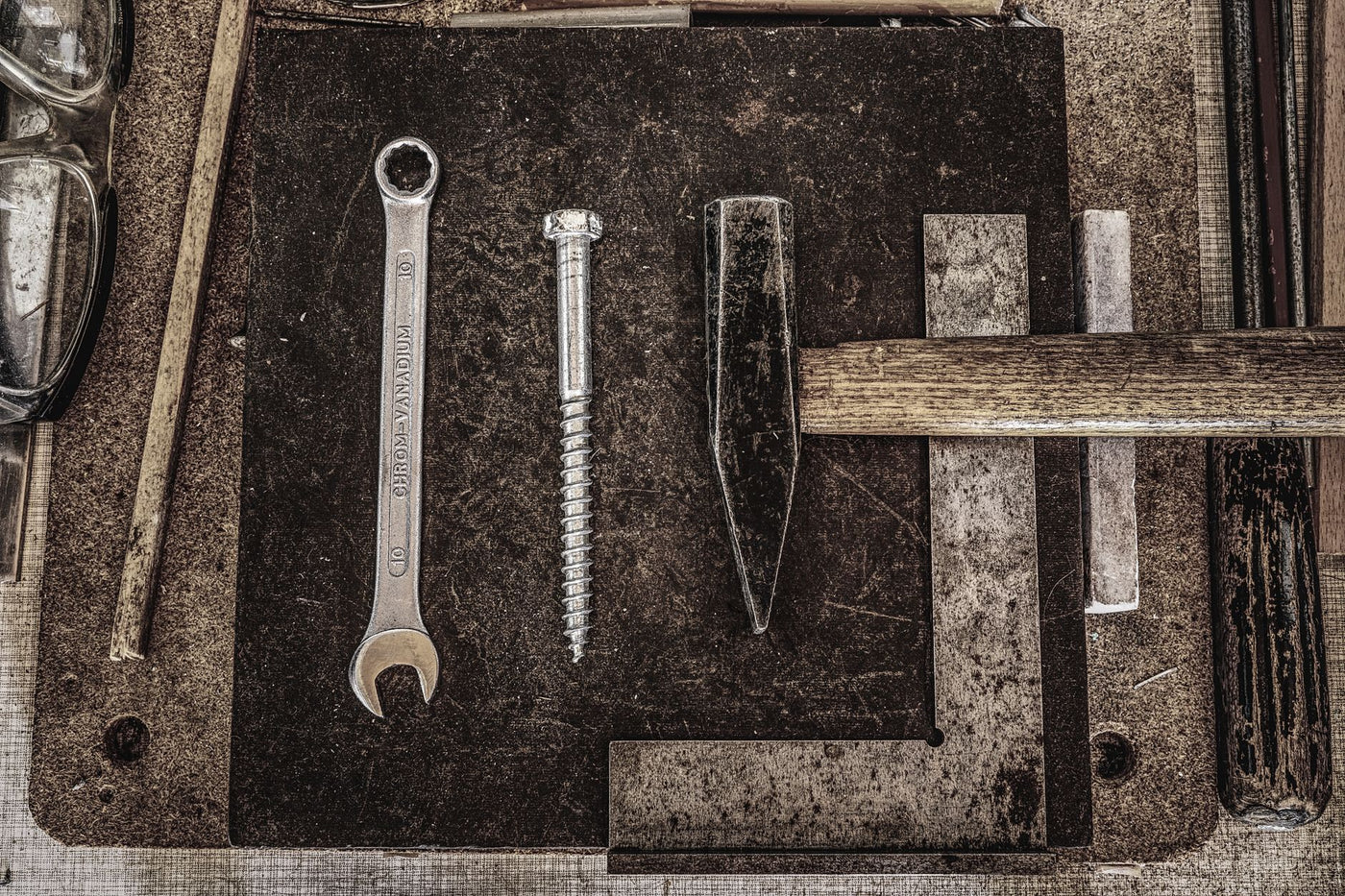 A collection of vintage workshop tools including a wrench, nail, and hammer displayed on a wooden table.