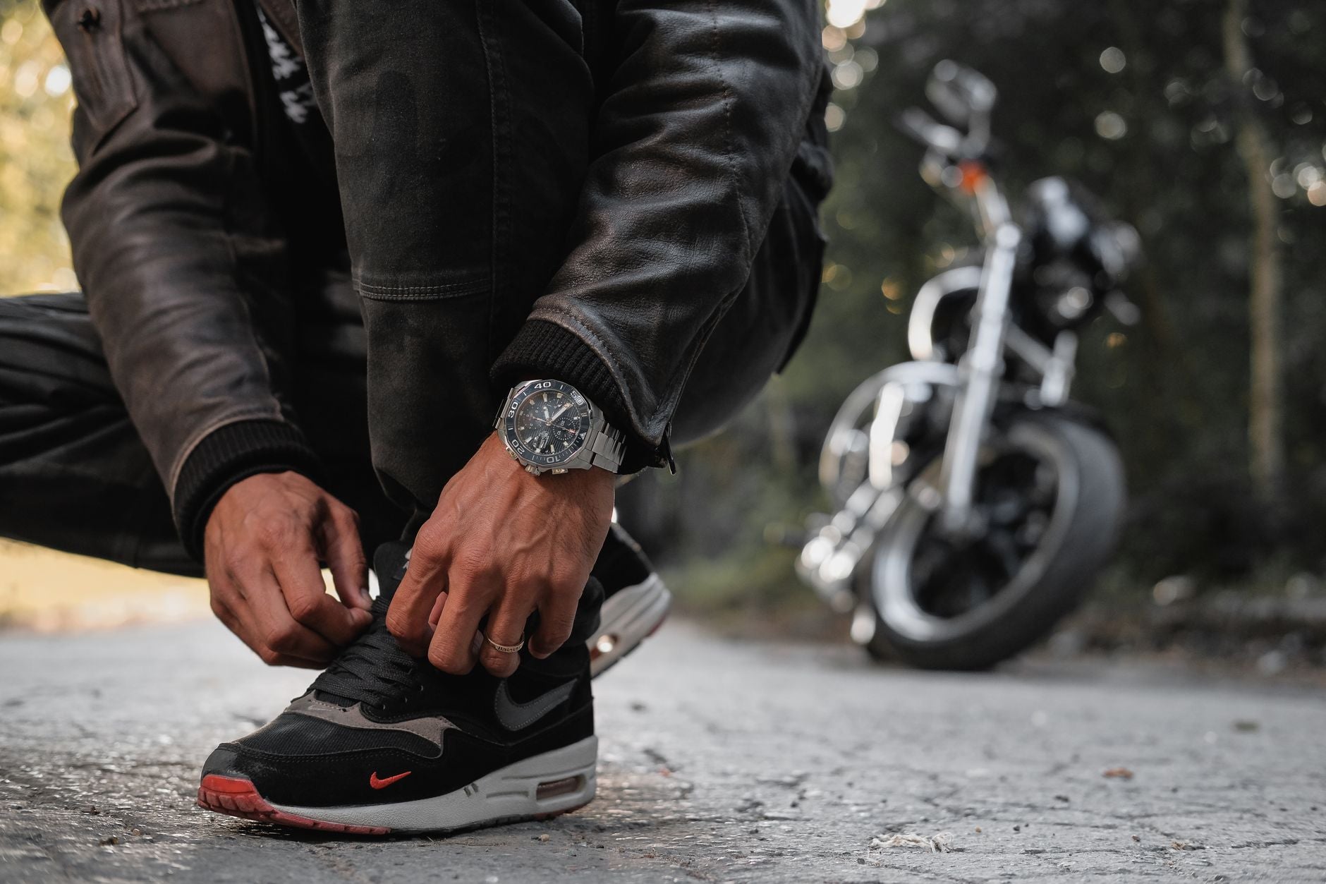Close-up of a motorcyclist tying shoes wearing a black leather jacket in an outdoor setting.