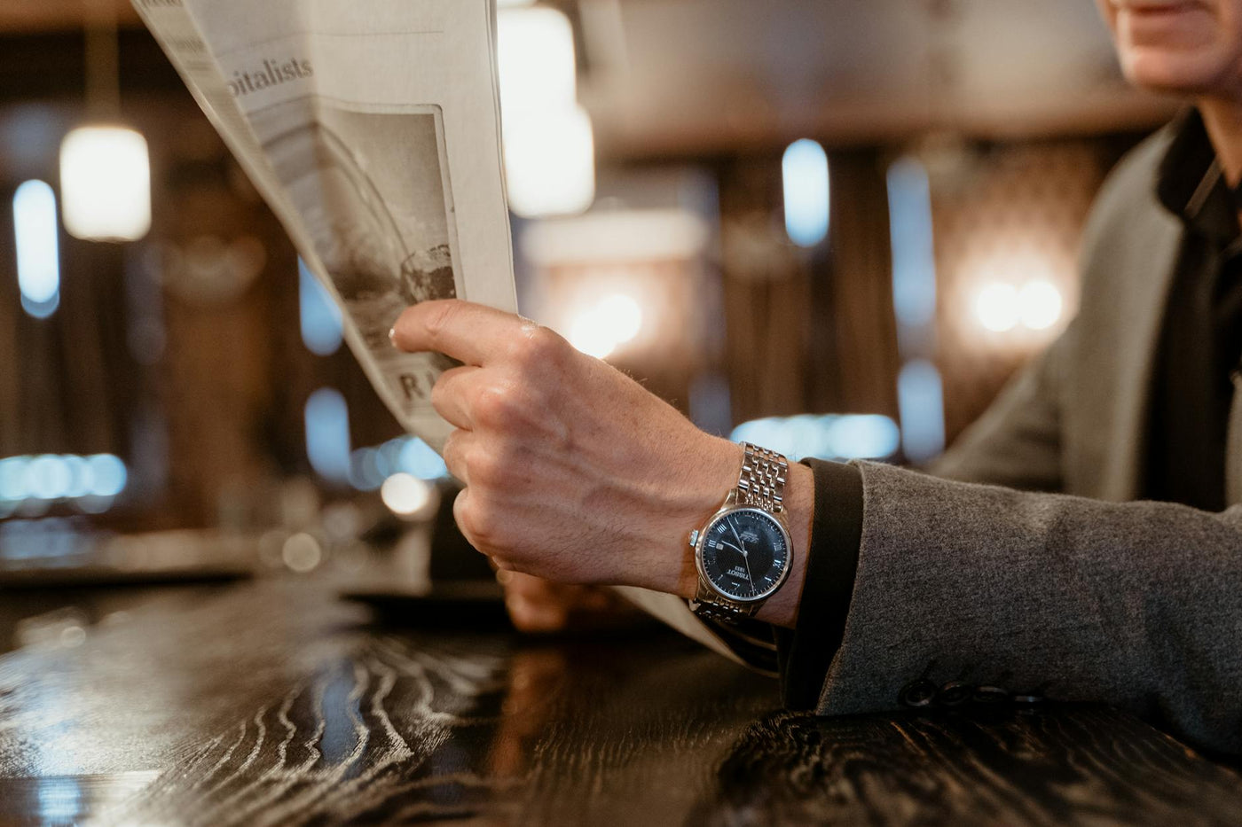 Close-up of a person's hand reading a newspaper in a cozy cafe, showcasing a classic wristwatch.